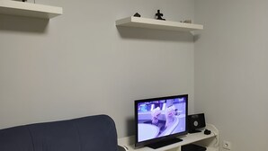 A living room with a dark blue sofa, a television on a white stand, and two white shelves with decorative items. - ORLANDO COSTA ADEJE (Costa Adeje)