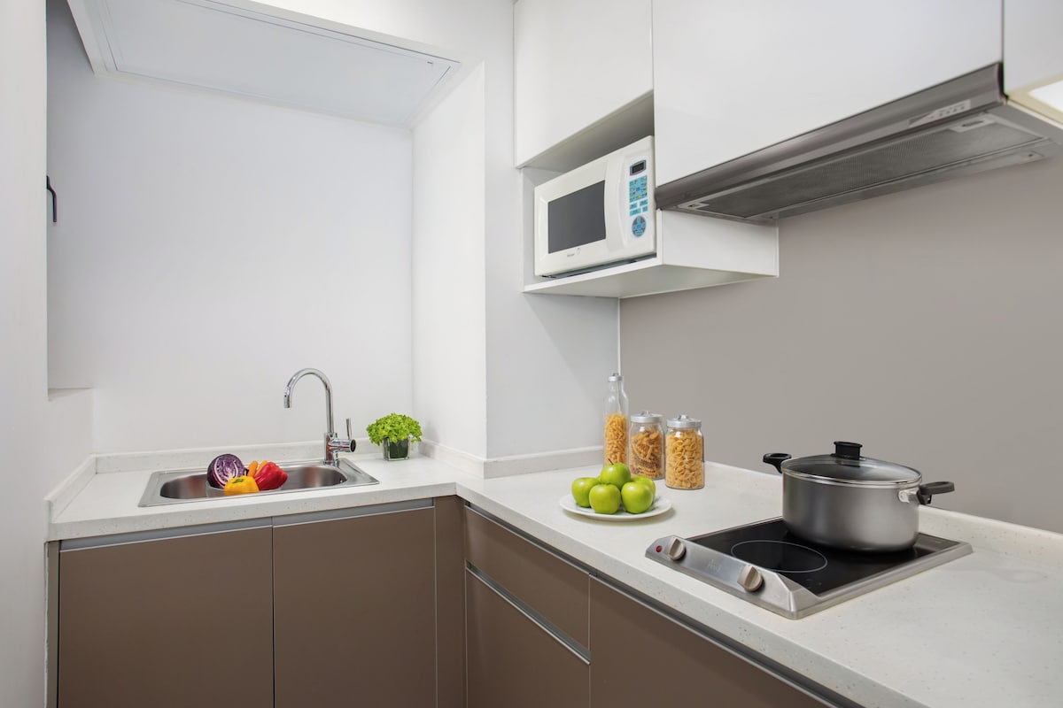 A modern kitchen with a stainless steel sink, a microwave, a stove, and a small potted plant.