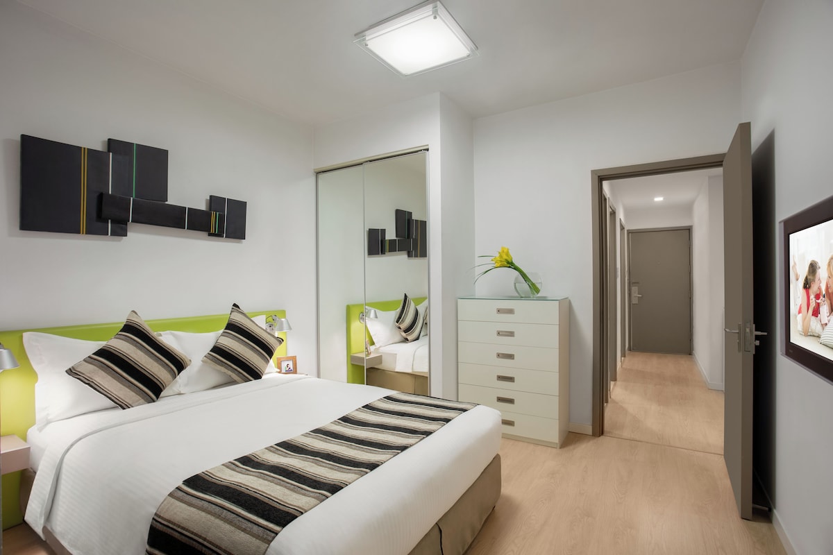 A modern bedroom with a bed, bedside tables, a dresser, and a mirror.