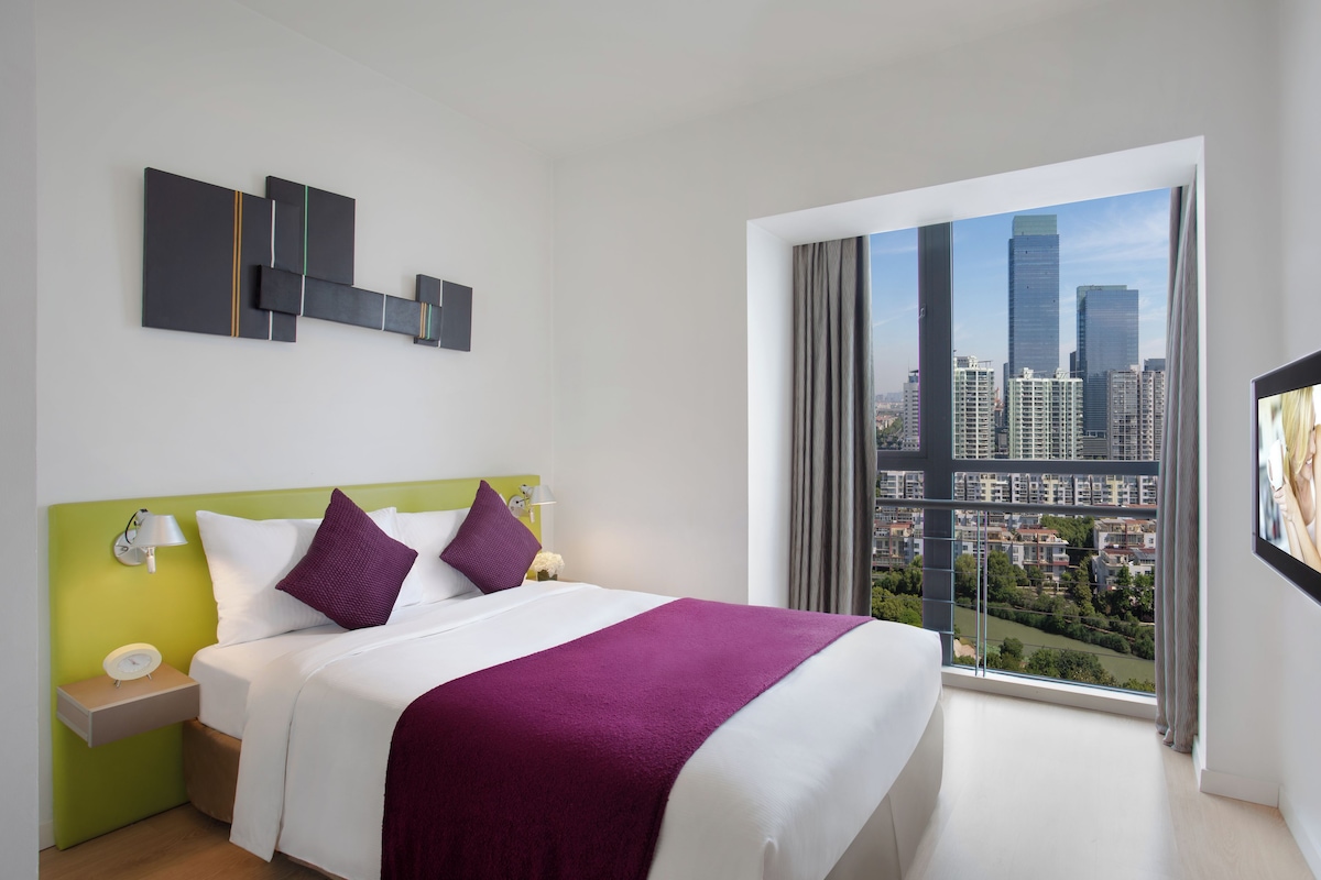 Una habitación de hotel moderna con una cama grande, vistas a la ciudad y una decoración minimalista.