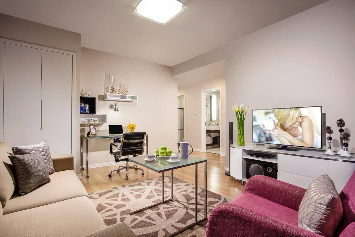 Ein modernes Wohnzimmer mit Sofa, Couchtisch, Fernseher und einer Küche im Hintergrund.