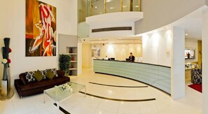 A modern hotel lobby with a reception desk, a sofa, a glass coffee table, and a large abstract painting on the wall. - Citadines Suzhou Xinghai (Suzhou)