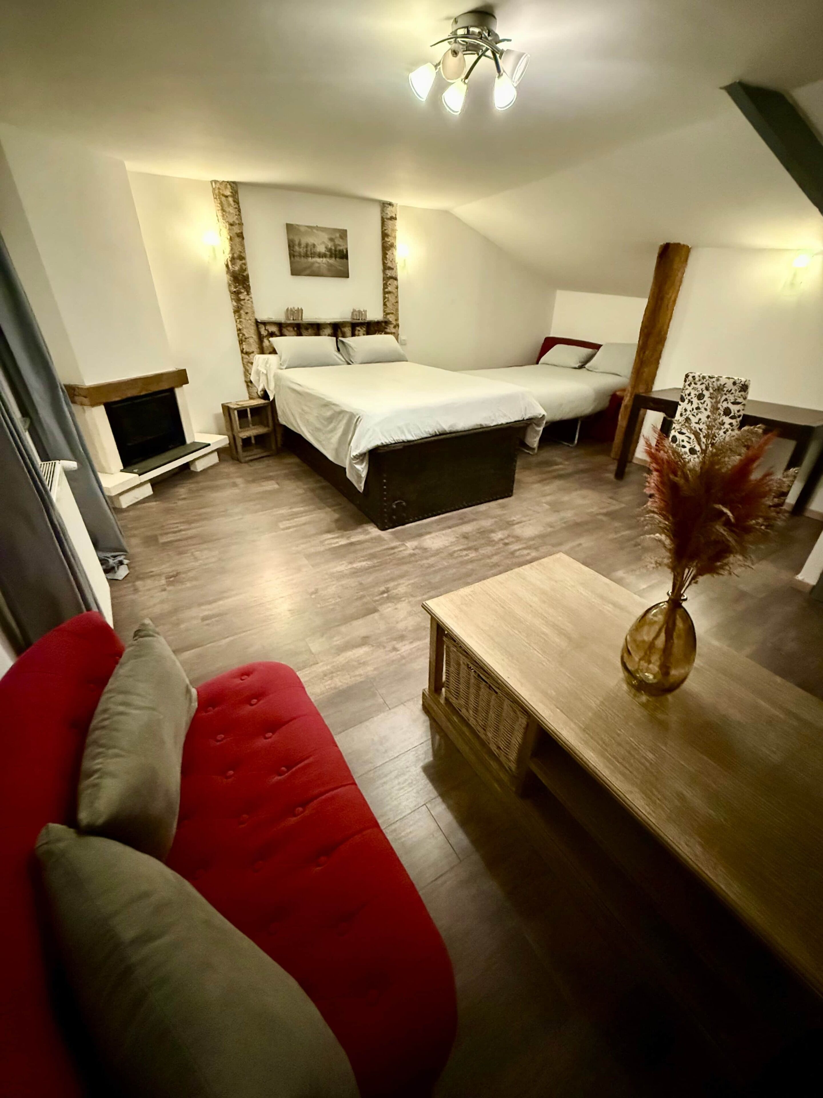 Kompakti hotellihuone, jossa on sänky, pieni sohva, puinen sohvapöytä ja takka.