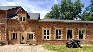 A brick building with a paved driveway and a vehicle parked in front. - La Laiterie Gite de groupe Proix (Proix)