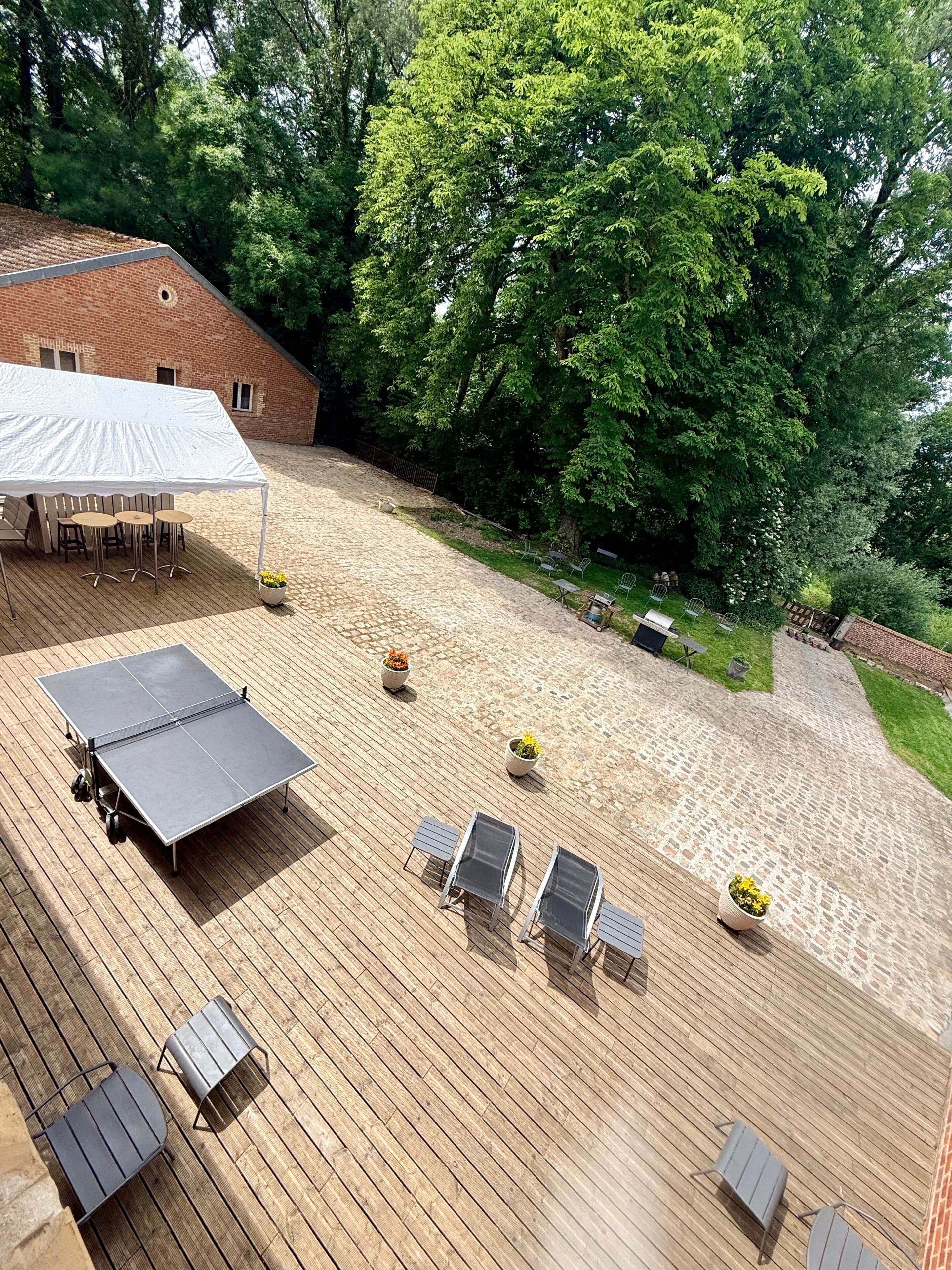 Een houten terras met buitenmeubilair, een tafeltennistafel en een overdekt gebied met stoelen.