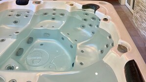 A hot tub with multiple jets, a wooden bench, and two potted plants. - La Laiterie Gite de groupe Proix (Proix)