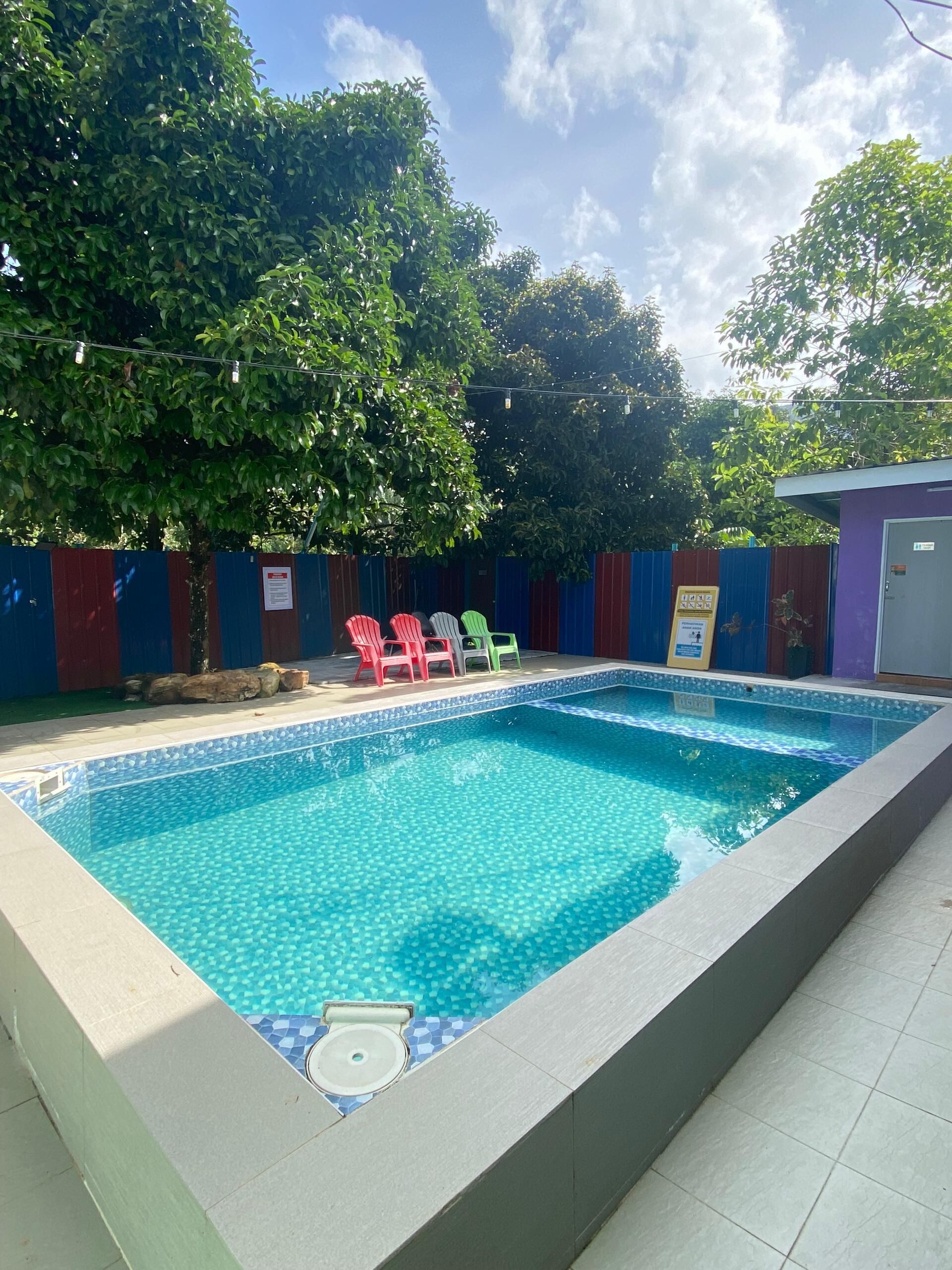 Una piscina rectangular con borde de azulejos y un desagüe pequeño en la esquina. Cuatro sillas de plástico de colores están dispuestas alrededor de la piscina.