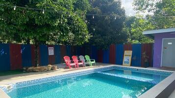 Una piscina rectangular con borde de azulejos y un desagüe pequeño en la esquina. Cuatro sillas de plástico de colores están dispuestas alrededor de la piscina.