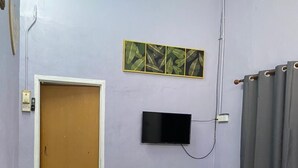 Ένα δωμάτιο με έναν κόκκινο καναπέ, μια τηλεόραση τοποθετημένη στον τοίχο, μια πόρτα και ένα παράθυρο με κουρτίνες.