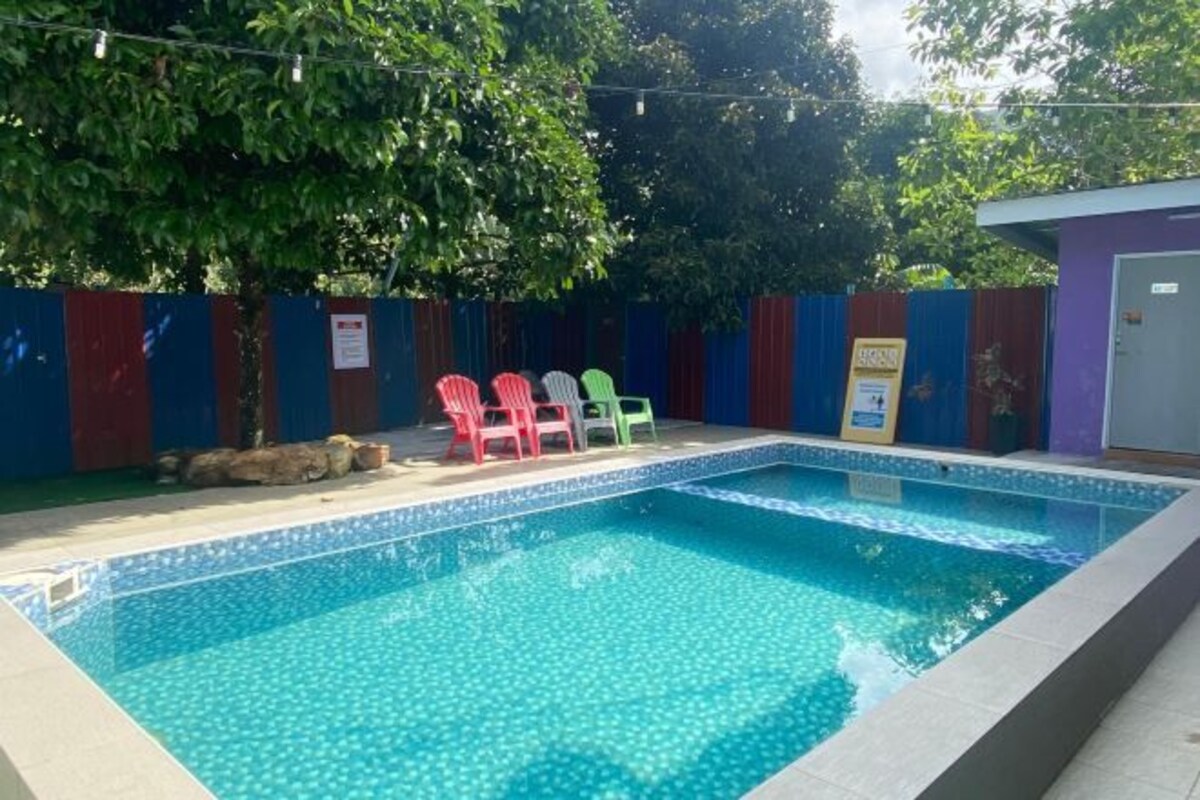 Une piscine rectangulaire dont le bord est recouvert de carreaux, entourée d’une clôture composée de panneaux rouges et bleus alternés.