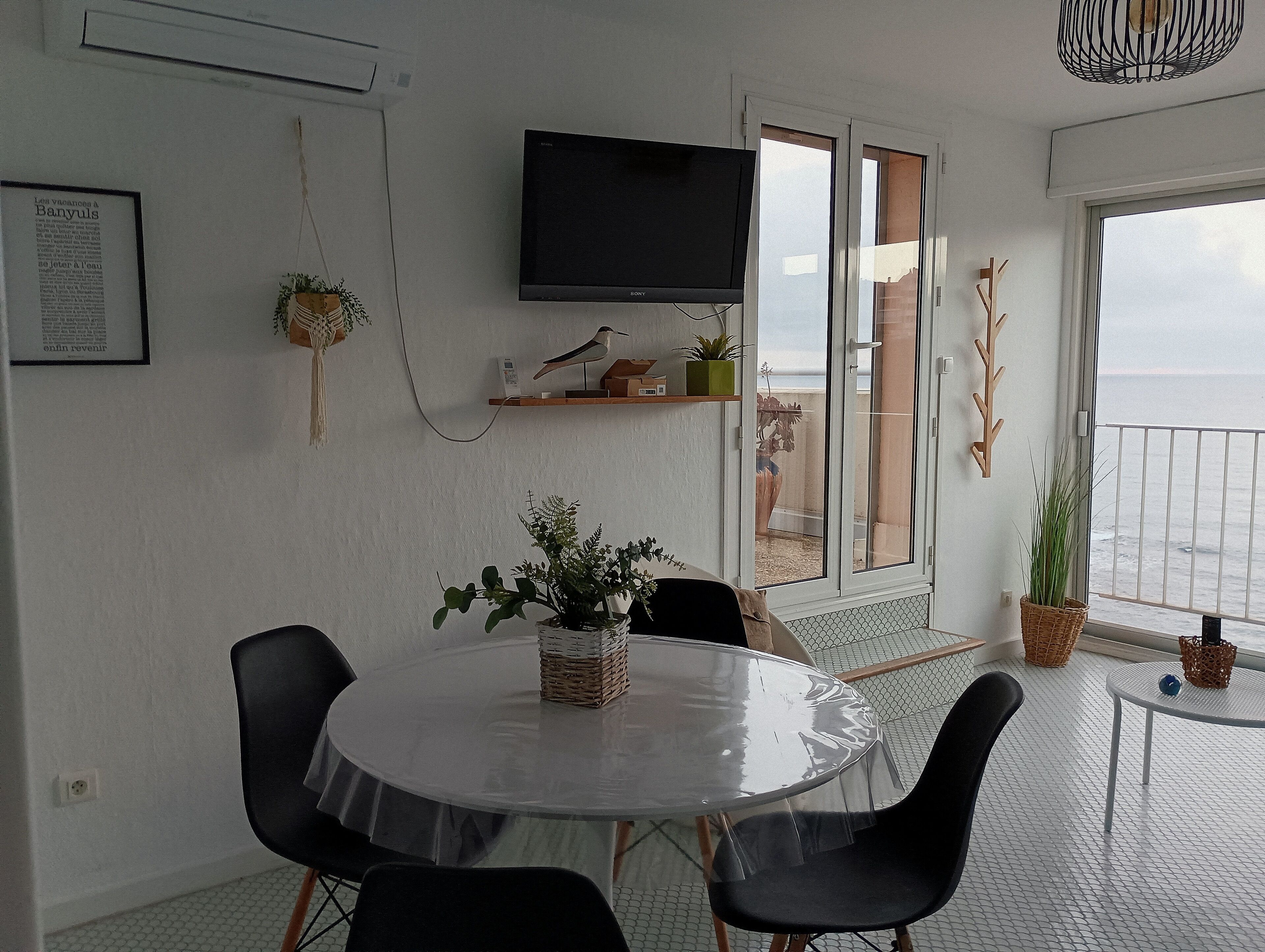 A modern living room with a round table, black chairs, a flat-screen TV, and a balcony with a view.