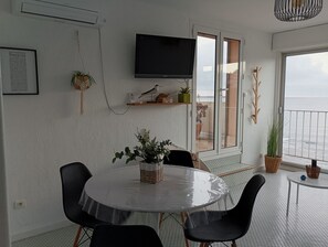 Uma sala de estar moderna com uma mesa redonda, cadeiras pretas, uma televisão de tela plana e uma varanda com vista.
