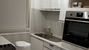 Cocina compacta con armarios blancos, horno empotrado, lavadora y cafetera.