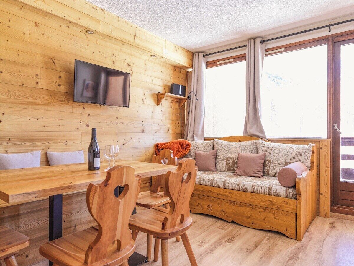 Ein Holzinnenraum mit einer Couch, einem Esstisch, Stühlen, einem an der Wand montierten Fernseher und einem Fenster mit Vorhängen.
