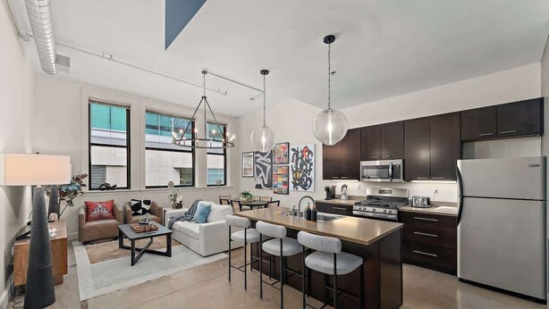 A modern kitchen with dark cabinets, stainless steel appliances, and a central island with bar stools.