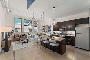 A modern kitchen with dark cabinets, stainless steel appliances, and a central island with bar stools. - Heart of PGH -  2BR Urban Oasis- Free Parking+GYM (Pittsburgh)