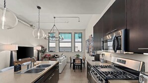 A modern kitchen with dark cabinets, stainless steel appliances, and pendant lighting.