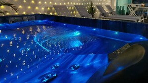 A hot tub with a blue-lit interior, surrounded by a wall of lights and a seating area with lounge chairs. - 2 minutes from the beach, pool, jacuzzi and parking included in a secure residence! (Les Trois-Îlets)