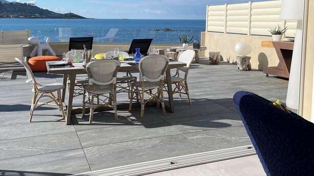 An outdoor patio with wicker furniture, a table with drinks, and a view of the sea. - The beach house (Calcatoggio)