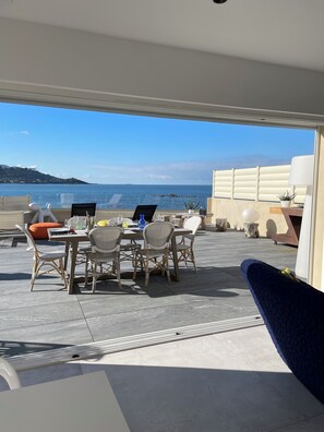 Une terrasse extérieure avec des meubles en osier, une table avec des boissons et une vue sur la mer.