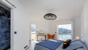 A modern bedroom with a large bed, a desk, and a view of the sea. - The beach house (Calcatoggio)