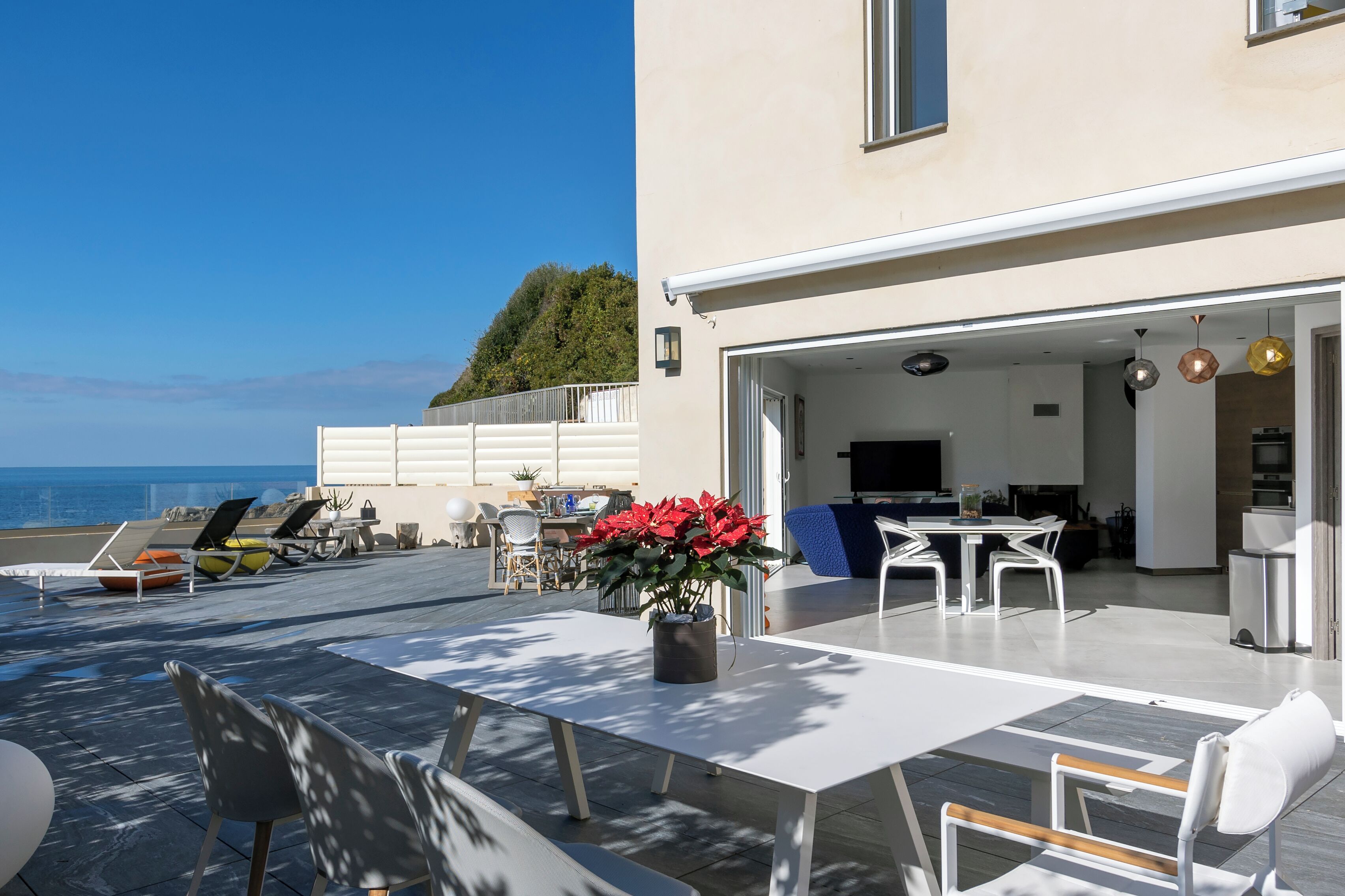 A modern outdoor patio with a dining area, seating, and a view of the sea.
