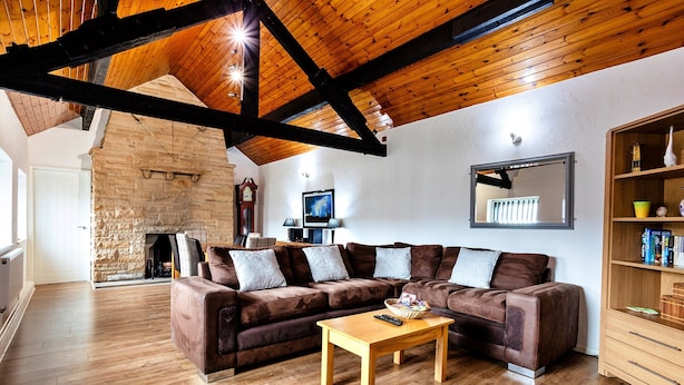 Sala de estar com lareira de pedra, vigas de madeira, sofá seccional e mesa de centro em madeira.