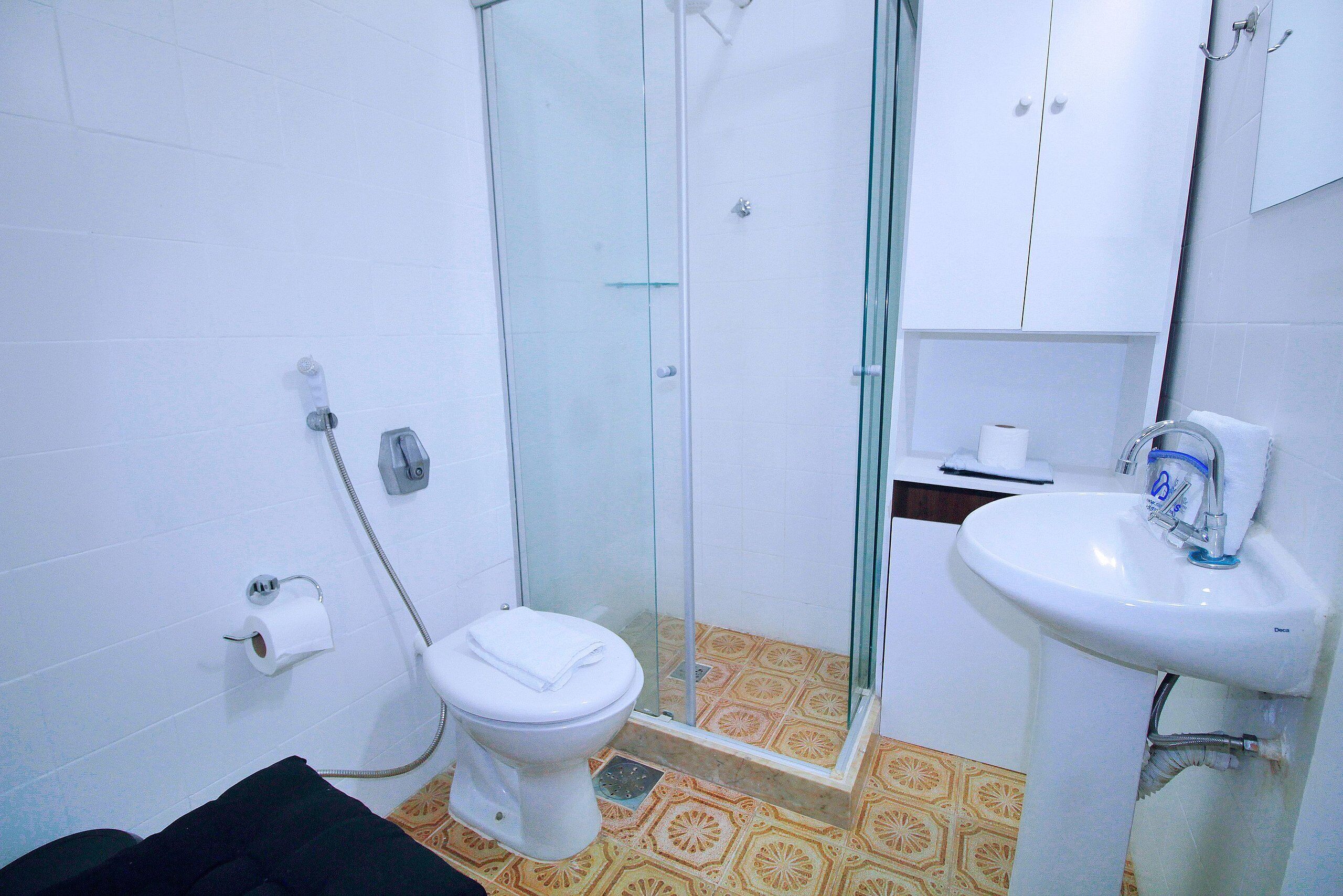 Een badkamer met toilet, een glazen douchecabine, een wastafel en vloertegels met een patroon.