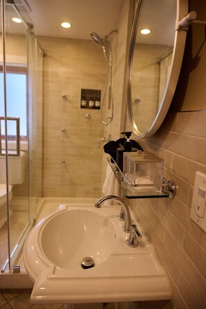 Een badkamer met een douchecabine van glas, een wastafel met spiegel en toiletartikelen op een plank.