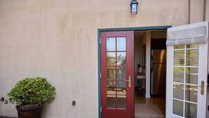 Una porta vermella amb un panell de vidre, una planta en test i una cuina visible a l'interior.