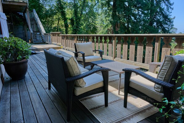 Een houten terras met rieten meubilair, een potplant en een houten trap naar een hoger niveau.