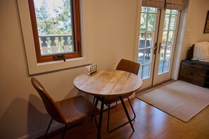 Een eetgedeelte met een ronde houten tafel, twee stoelen, een raam en een deur naar een buitenruimte.