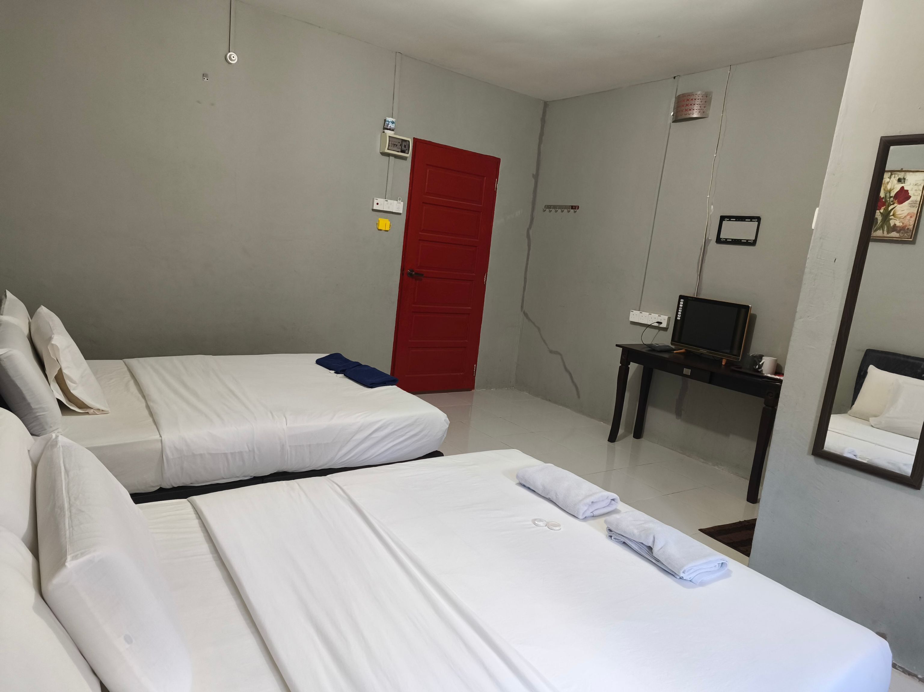 Habitación de hotel con dos camas, una puerta roja, un televisor sobre una mesita y un espejo en la pared.