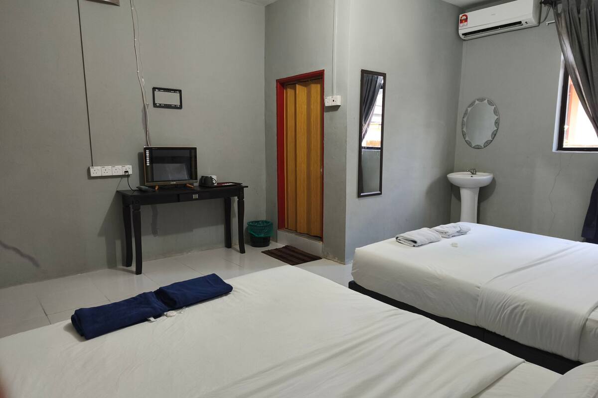 Ett hotellrum med två sängar, ett skrivbord med en dator, en spegel, ett handfat och en luftkonditioneringsanläggning.