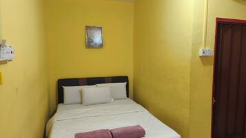 A small, yellow-walled room with a single bed, a red-framed door, and a wall-mounted light switch.