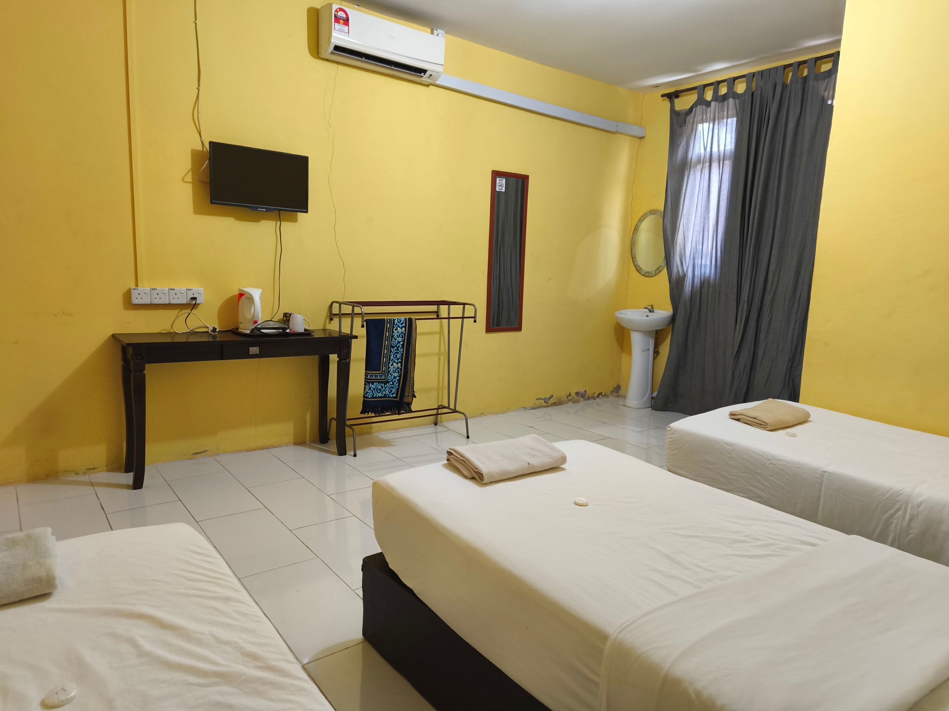 A hotel room with two beds, a desk with a computer, a wall-mounted TV, a sink, and a window with curtains.