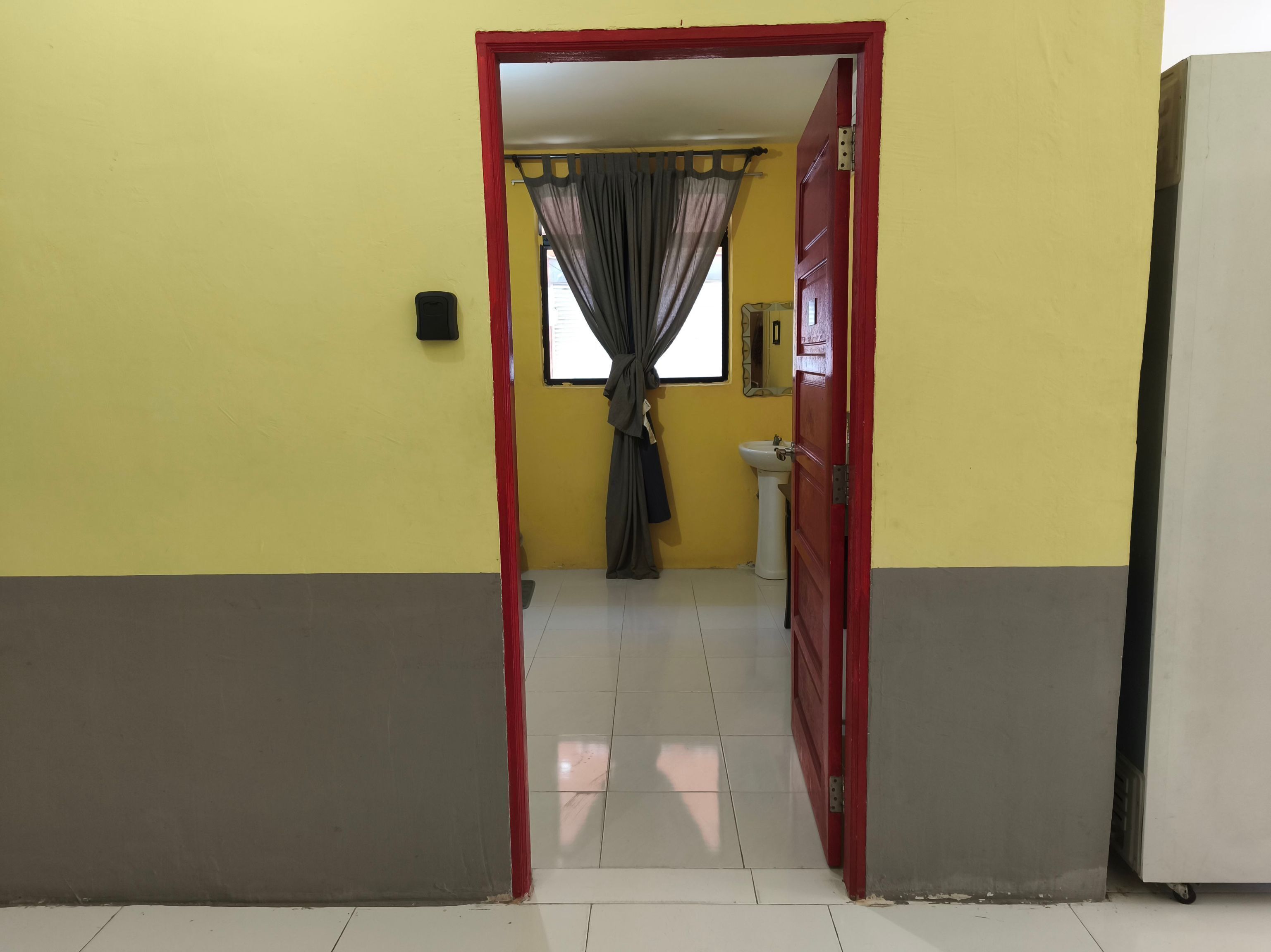 A hallway with a red door leading to a room with a window and a sink.