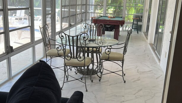 Een ruime kamer met een glazen tafel en stoelen, een plafondventilator en grote ramen met uitzicht op de omgeving.
