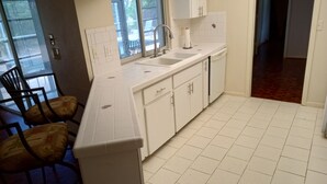 Een keuken met witte kastjes, een spoelbak en een aanrecht. Er staan stoelen en een eettafel.