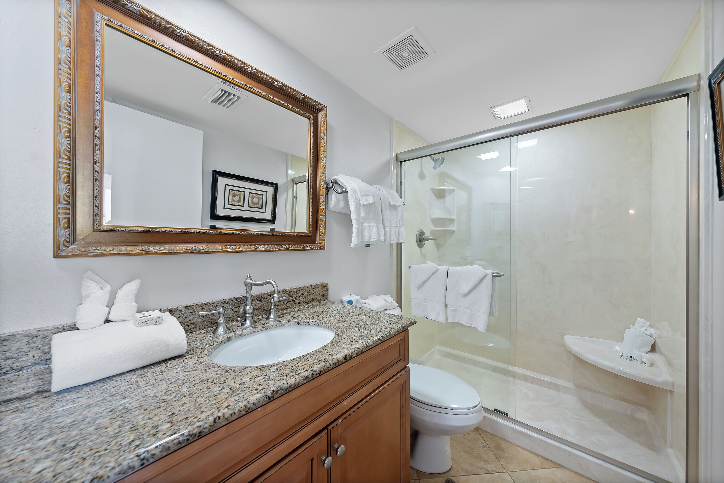 A bathroom with a granite countertop sink, a large mirror, a toilet, and a glass-enclosed shower.