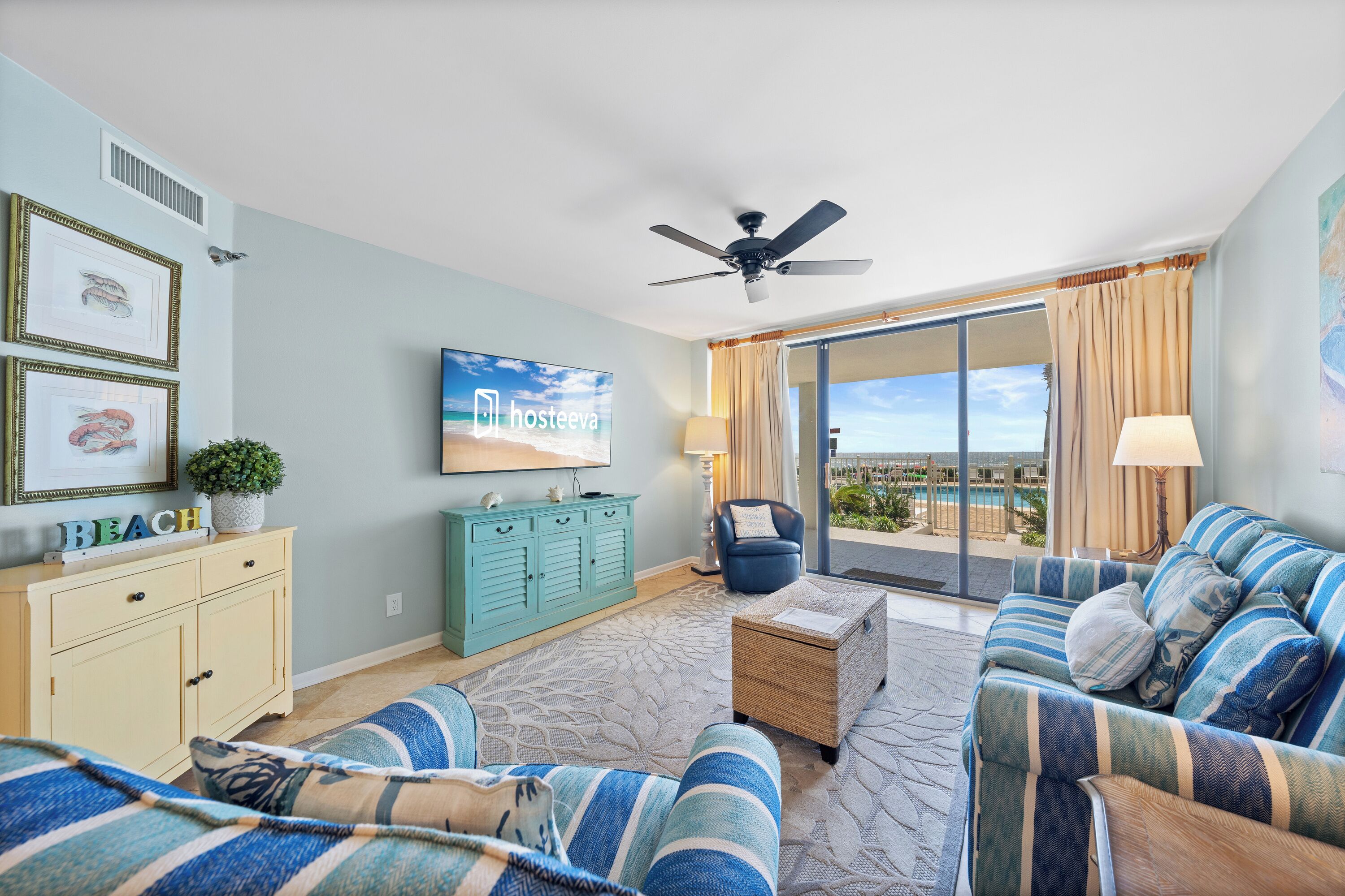 A hotel room with a large window, a ceiling fan, a TV, a sofa, a small table, and a cabinet.