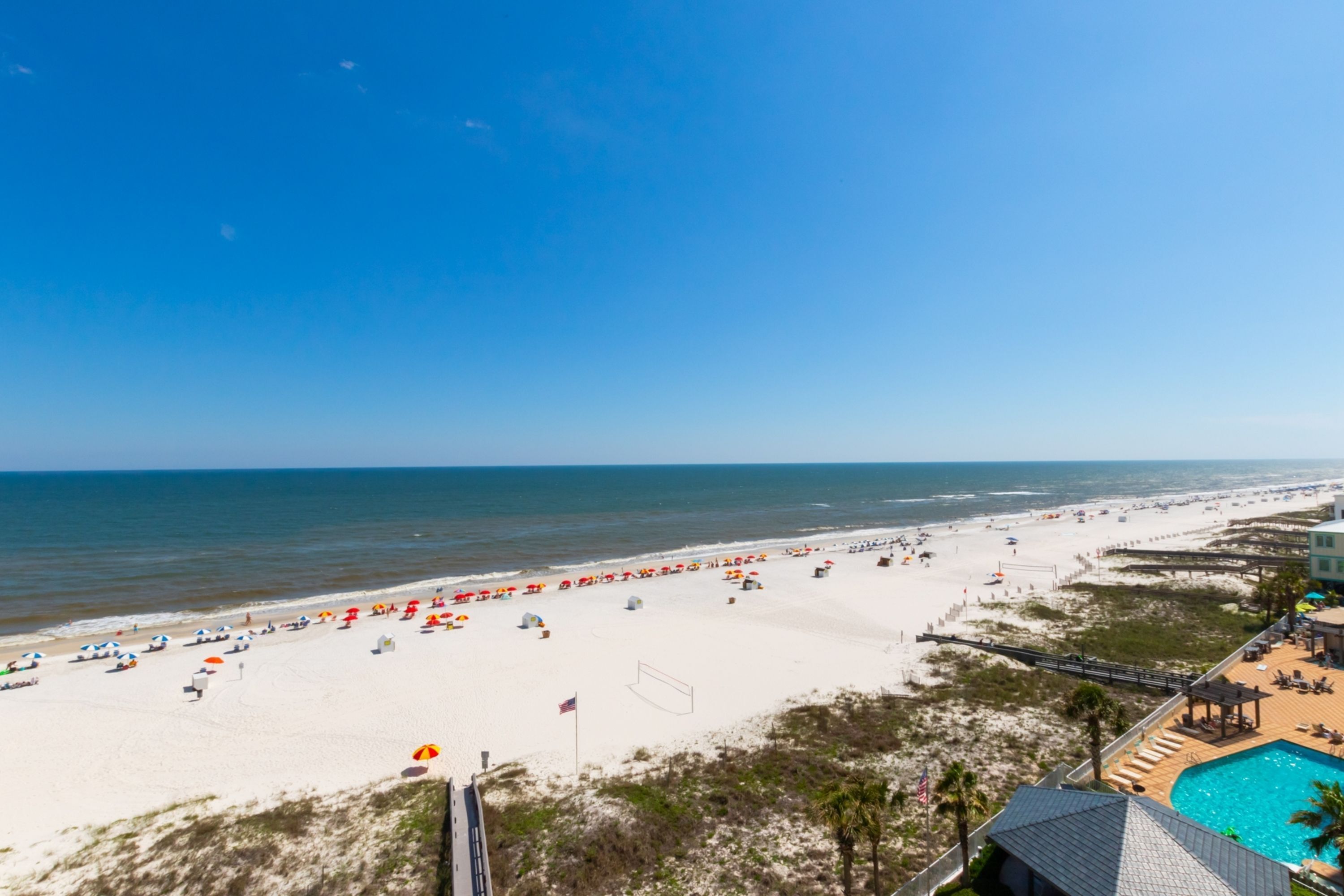 Ett semesterhotell vid stranden med en swimmingpool, parasoller och en strandpromenad.