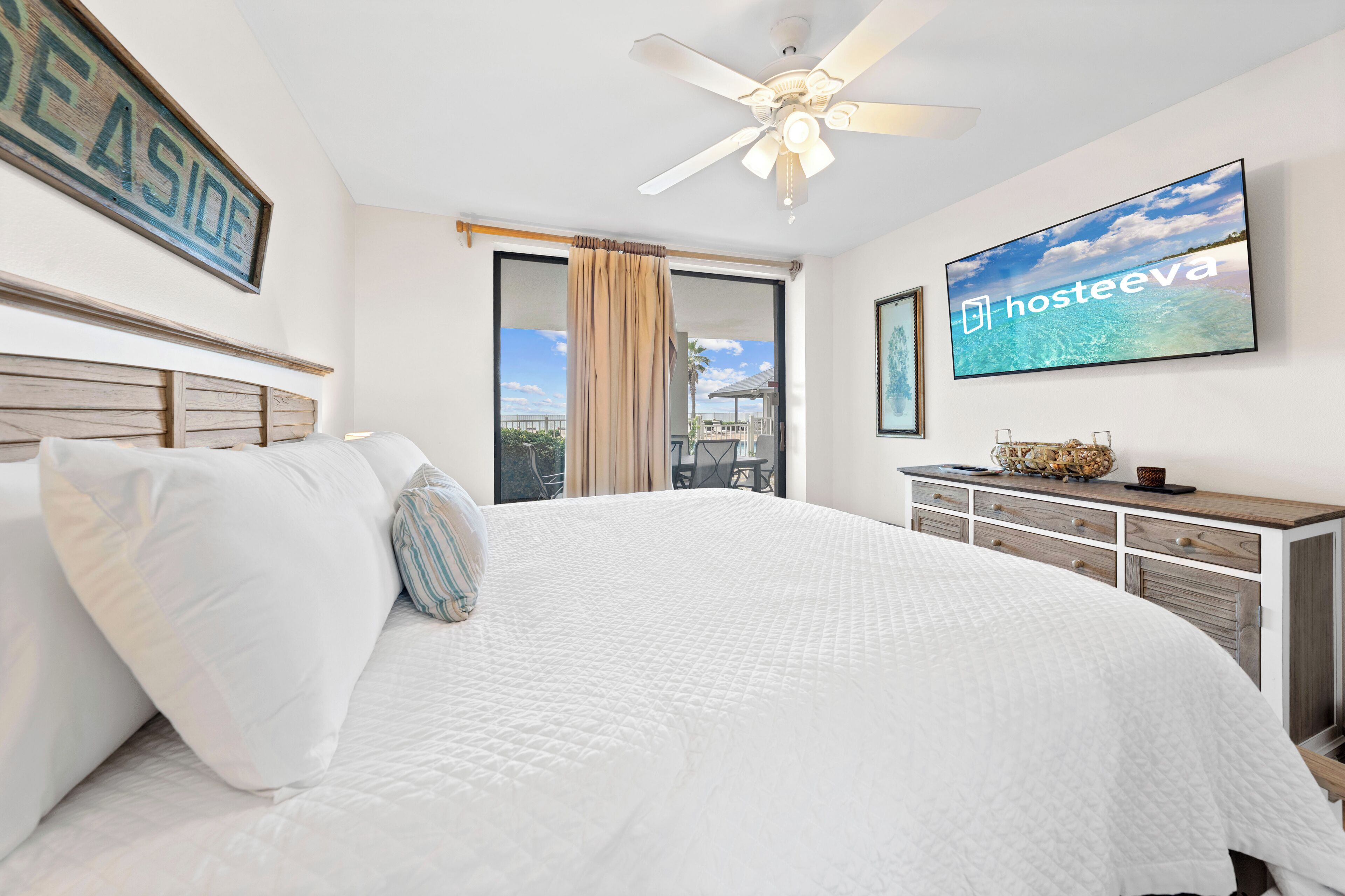 A hotel room with a large bed, a ceiling fan, a TV, and a view of the outdoors.
