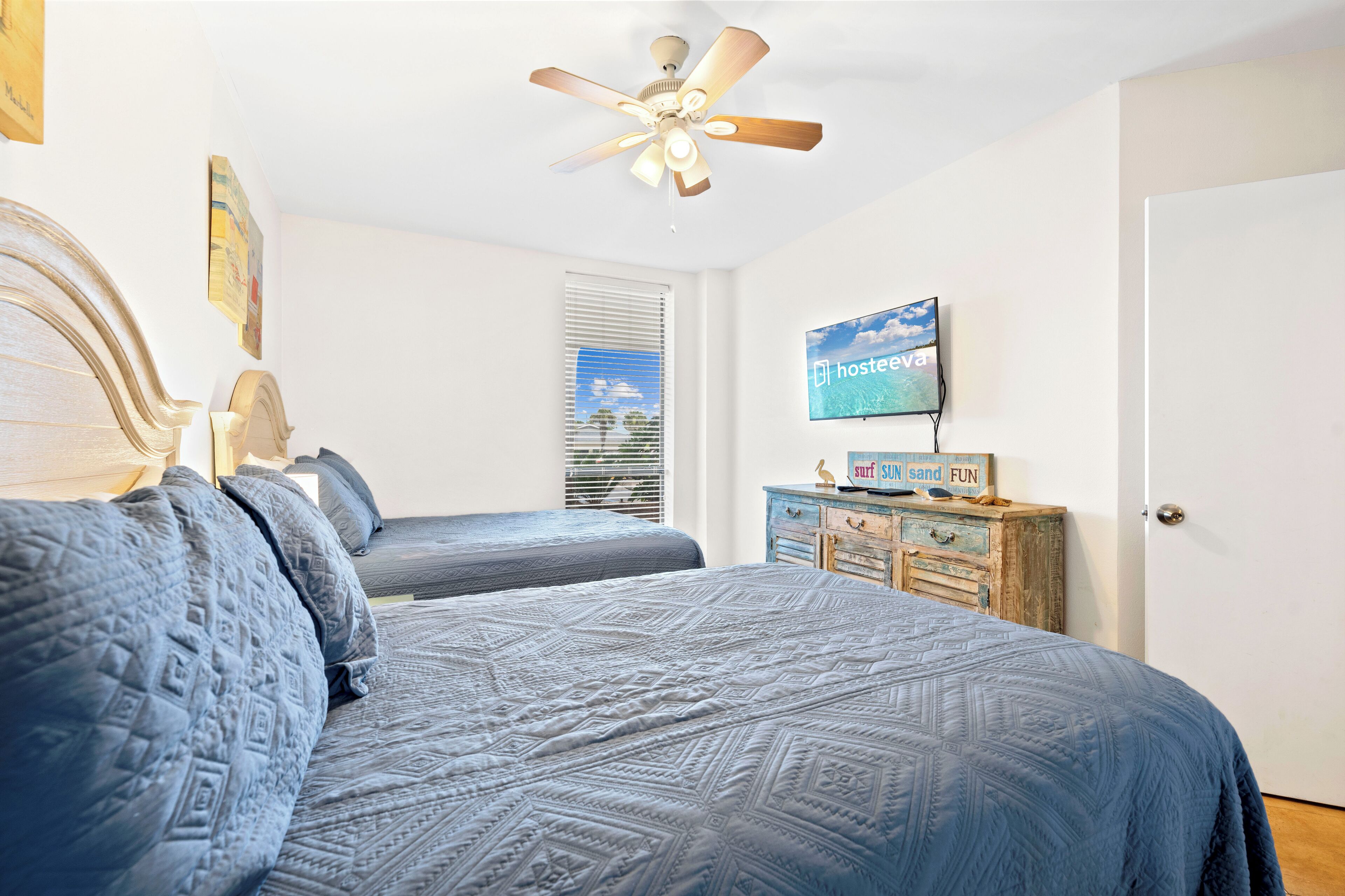 A bedroom with two beds, a ceiling fan, a television, and a dresser with a sign.