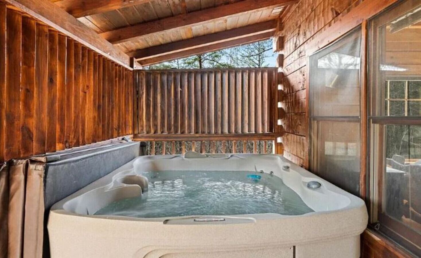 Una cabaña de madera con un jacuzzi bajo un porche cubierto.