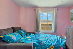 A bedroom with a bed, a window with curtains, a radiator, and a wall-mounted light switch.
