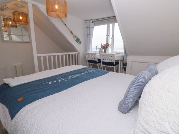 Ein Schlafzimmer mit Bett, Schreibtisch und Stuhl. Es gibt ein Fenster mit Vorhängen, eine Heizung und eine Deckenleuchte.