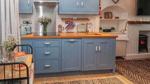 A kitchen with blue cabinets, a wooden countertop, a stove, and a patterned rug. - Seahorse Cottage (St Ives)