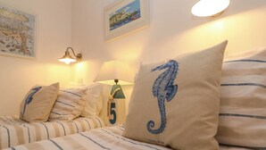 A hotel room with striped bedding, a seahorse pillow, a lamp, and wall art. - Seahorse Cottage (St Ives)