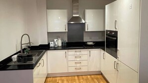 A modern kitchen with white cabinets, a black countertop, a stainless steel range hood, and a built-in oven. - Dartford Apartment - Sleeps 3 - Central Stay (Dartford)